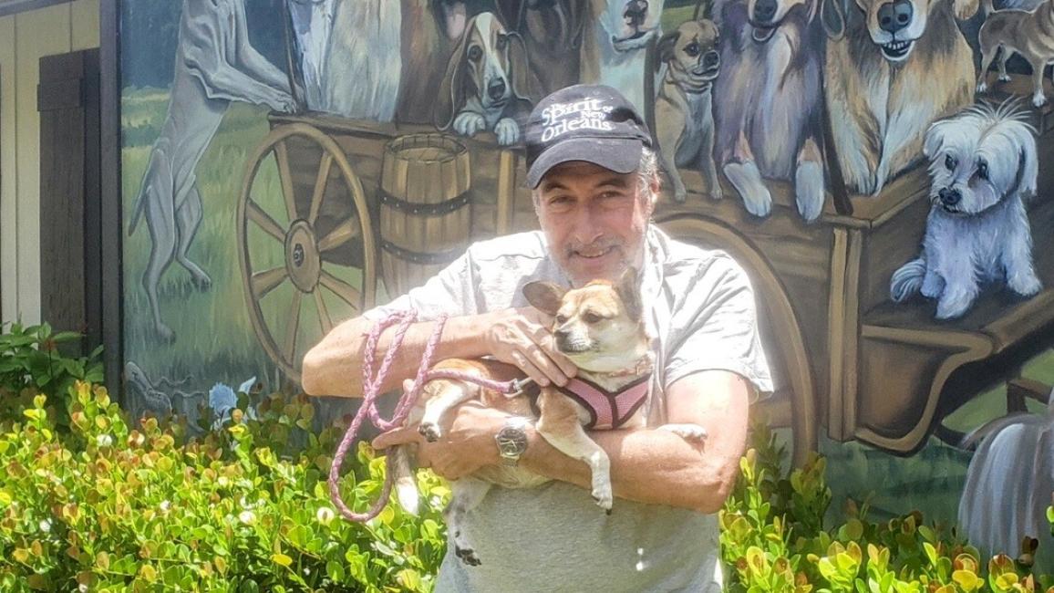 Gary Slusher holding the Chihuahua-corgi mix he adopted in front of a mural featuring dogs in a covered wagon